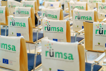 Jutebeutel bedruckt mit dem RÜMSA-Logo hängen über Stuhllehnen